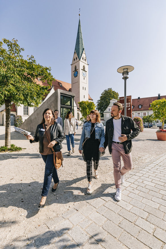 Eine Stadtführerin führt Gäste über den St.-Mang-Platz