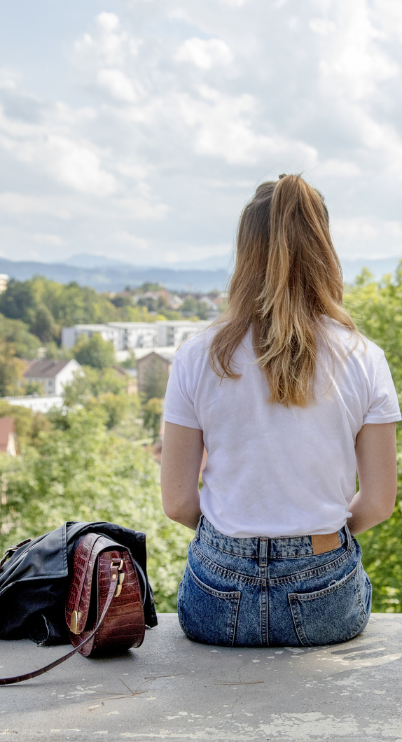 Frau sitzt auf einer Mauer und genießt den Ausblick