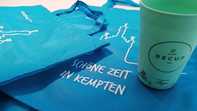 Die hellblaue Kempten-Tasche und ein Recup Becher Allgäu