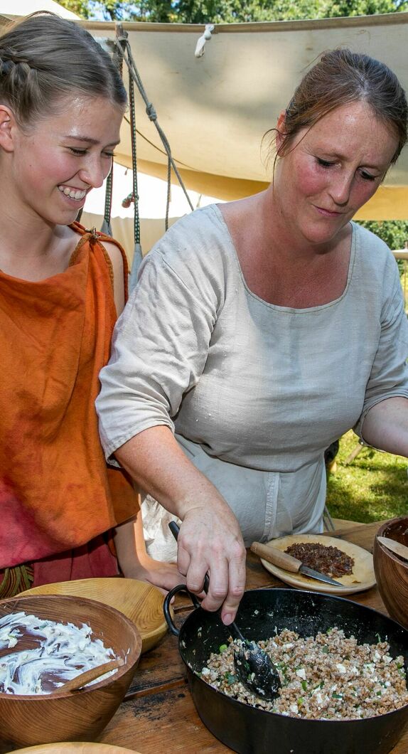 zwei Damen in Römischen Gewand bereiten eine Mahlzeit zu